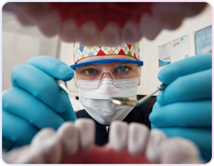 Crown 2 Dokter gigi dengan masker, kacamata pelindung, dan sarung tangan biru memeriksa gigi pasien dari sudut pandang pasien