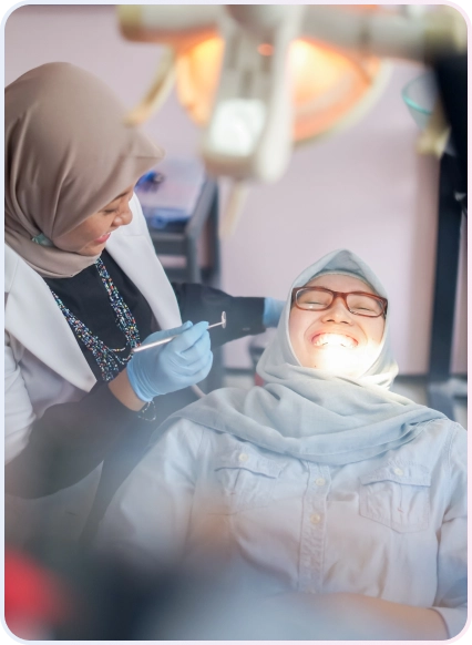 Service Aligner 17 Dokter gigi wanita memeriksa gigi pasien wanita berjilbab yang tersenyum lebar di bawah lampu dental, menunjukkan perawatan gigi yang nyaman dan menyenangkan.