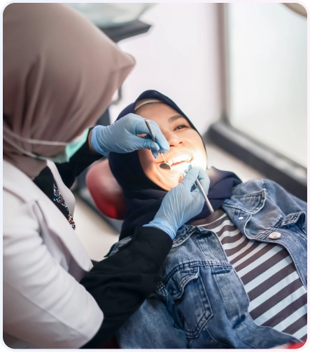 Service Behel 4 Dokter gigi wanita berjilbab sedang memeriksa gigi pasien wanita berjilbab yang tersenyum di kursi dental klinik.