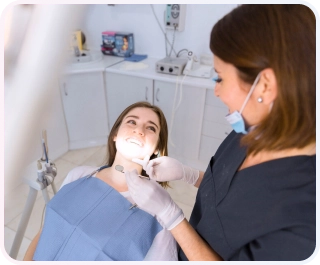 Perawatan Saraf Gigi 6 Pasien wanita tersenyum cerah di kursi dental saat dokter gigi wanita memeriksanya, menunjukkan pengalaman yang nyaman